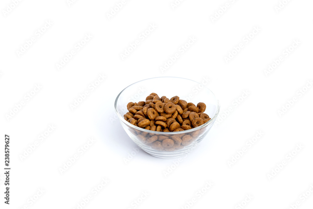 Dry cat food ringlets poured into a glass bowl on a white background. Dry cat food ringlets poured into a glass bowl on a white background.