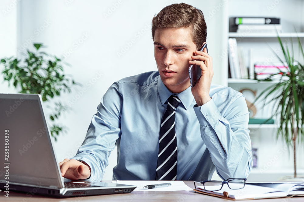 Worker talking on the phone and looks at the laptop. Photo of successful manager working with financial data in the office. Business concept Worker talking on the phone and looks at the laptop. Photo of successful manager working with financial data in the office. Business concept