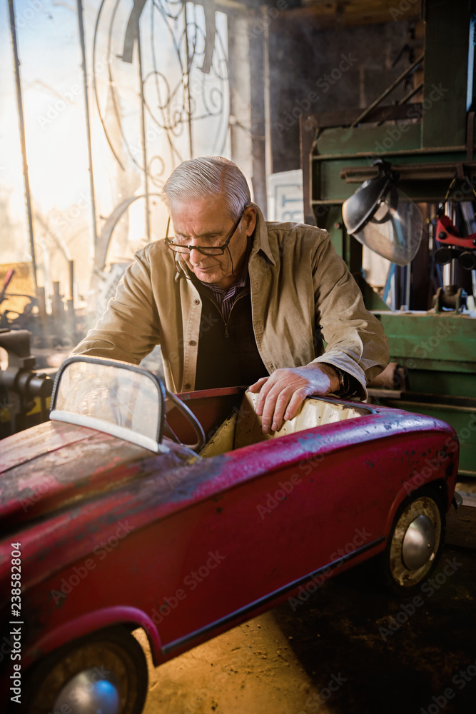 Senior man in his workshop repairing an old fashioned pedal car