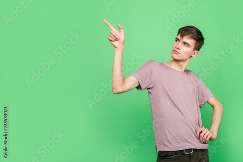 Stylish guy in t-shirt shows his finger to the side standing on a green