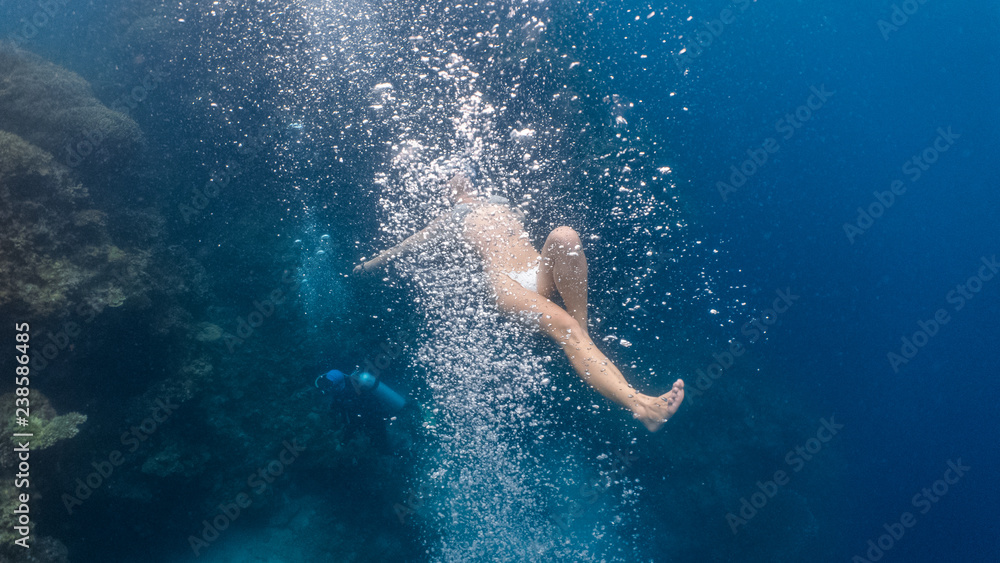 Woman in bikini plays with scuba bubbles underwater