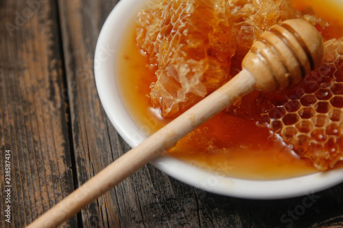 Honey with honeycomb in a white ceramic plate on rustic wooden table