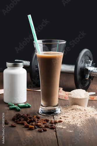 Protein shake, vitamins bottle, black dumbbells and raisins
