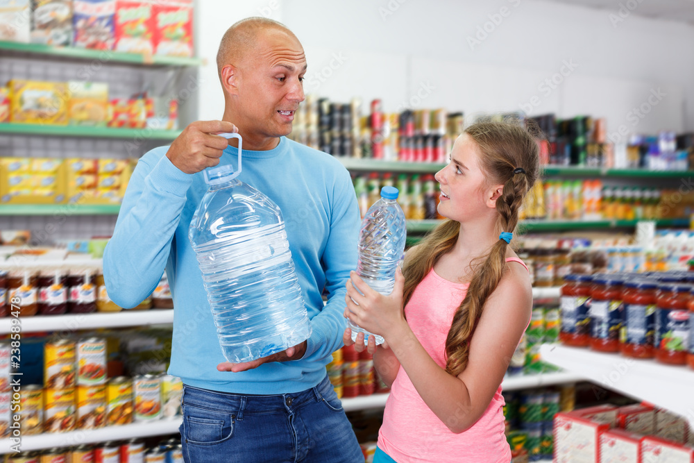 family of cheerful father and tween daughter buying still water in supermarket