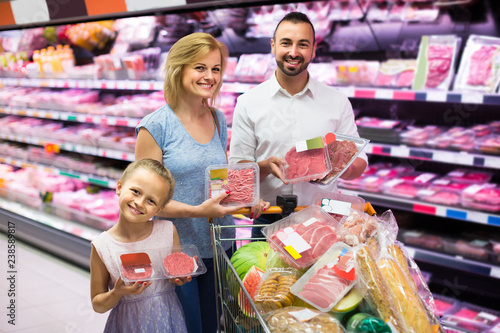 parents with daughter choosing meat in refrigerated section in hypermarket