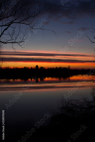 Croatia, nature park Lonjsko polje, beautiful red sunset over Sava river in autumn, reflection on water