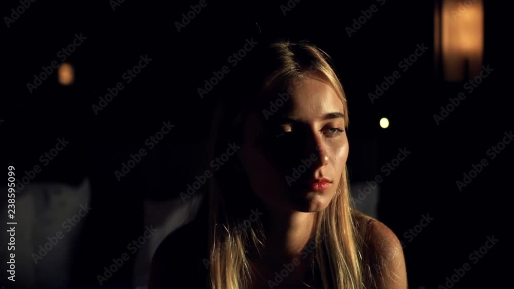 In dark face portrait of young caucasian pretty blond hair woman posing look at camera on living background beautiful closeup cute girl home caucasian color romantic turning portrait slow motion In dark face portrait of young caucasian pretty blond hair woman posing look at camera on living background beautiful closeup cute girl home caucasian color romantic turning portrait slow motion