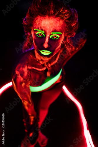 Portrait of a beautiful young sexy girl with ultraviolet paint on her body. Pretty woman with glowing bodyart in black lamp light