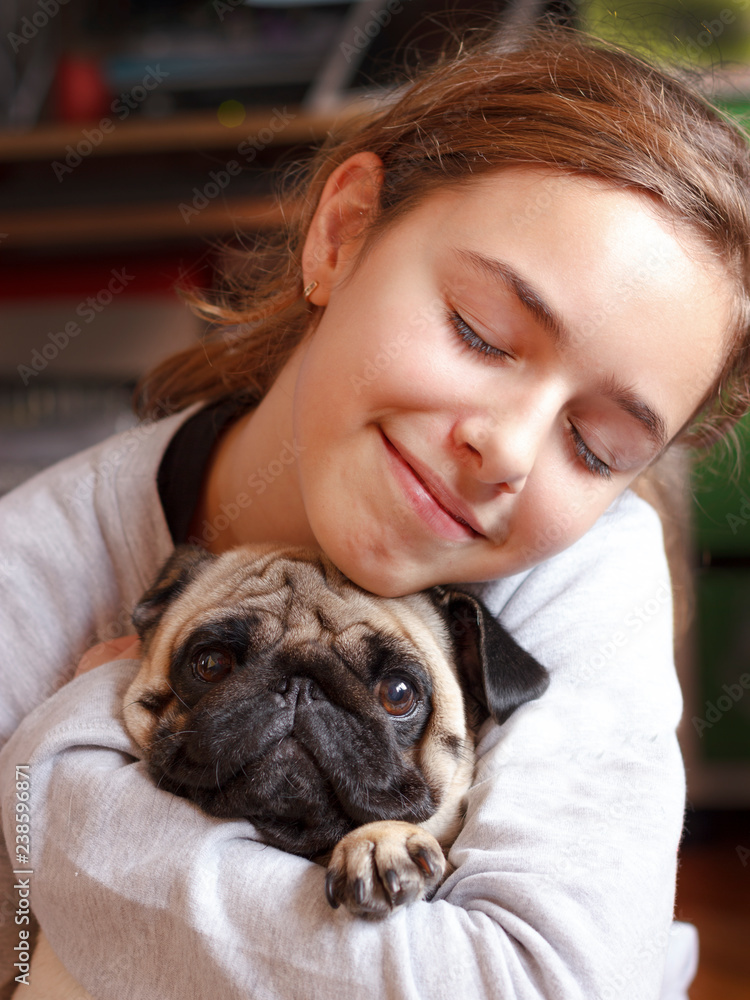 Fototapeta Szczęśliwa ładna uśmiechnięta nastolatka przytulająca mopsa z miłością