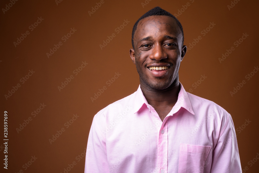 Fototapeta premium Portrait of young African businessman smiling against brown background