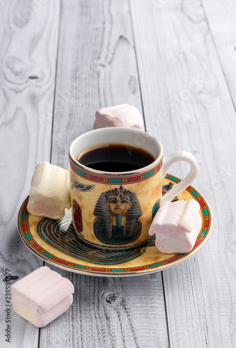 A Cup of coffee with Egyptian patterns and sweet marshmallows on a light wooden background