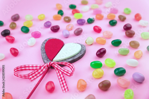 Jelly bean sweets and a festive crafted heart on pink background. Love and St Valentine's Day concept