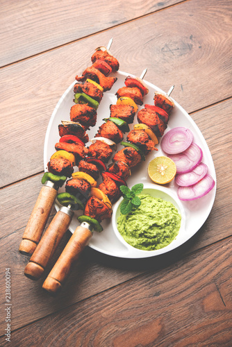 grilled chicken tikka on skewers. served in a plate with green chutney and onion. Selective focus