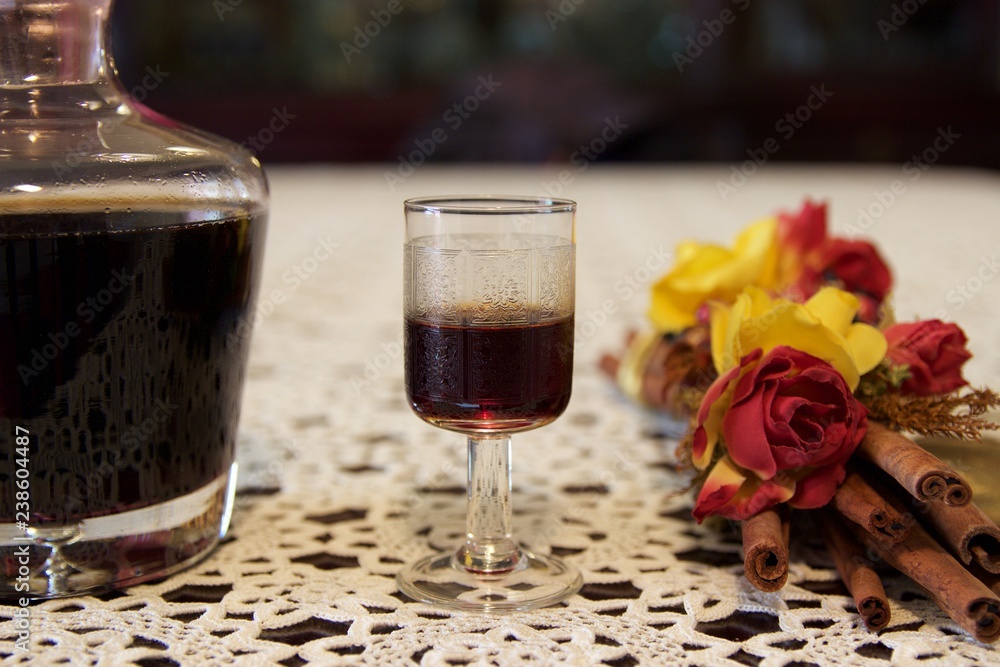 Cherry alcohol liqueur beverage in retro small engraved small glass bouquet cinnamon sticks with dry flowers red yellow roses isolated on white handmade embroidery on a black table