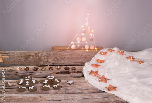 Lebkuchenmännchen liegen mit bronze farbigen Christbaum Anhängern auf einem weißen Lammfell. Das Fell liegt auf alten Holzbalken. Rosé goldene Lichterkette mit Sternen. photo