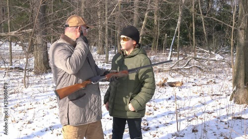 A father teaching his son how to shoot a shotgun safely in the woods in winter