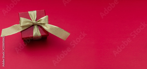 Red gift box with gold ribbon on red background, view from above, copy space