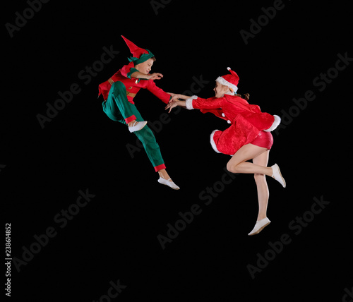 Christmas time, childhood, fairy tale. Cheerful kids - A young girl wearing a Santa's costume and boy wearing elf costume flying together photo