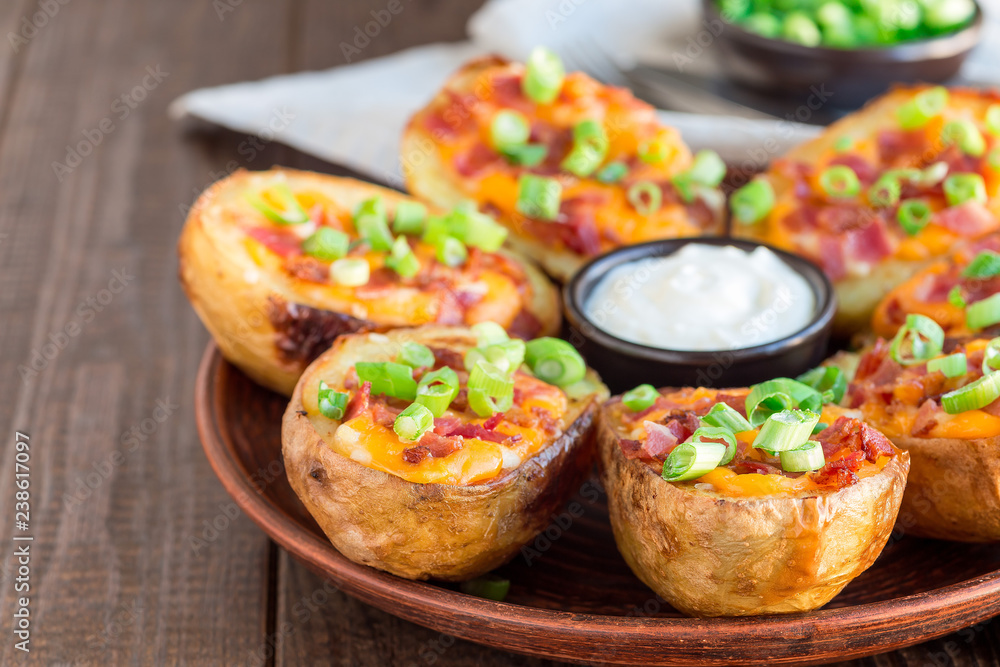Baked loaded potato skins with cheddar cheese and bacon, garnished with scallions and sour cream, horizontal copy space Baked loaded potato skins with cheddar cheese and bacon, garnished with scallions and sour cream, horizontal copy space