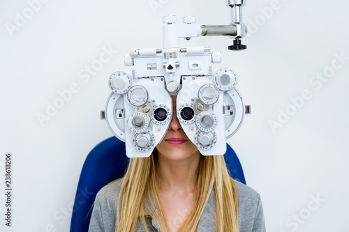 Pretty young woman doing eyesight measurement with optical phoropter in ophthalmology clinic. photo