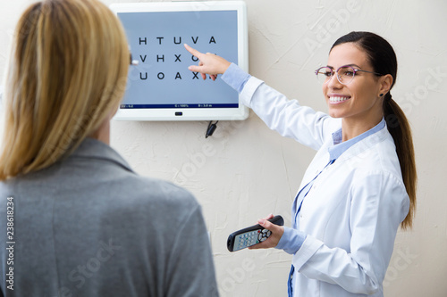 Beautiful optician doing eye test with eye chart on her patient in ophthalmology clinic.
