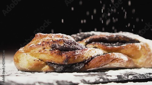 Swirl bun with poppy seeds, sprinkled with flour, slow motion. Poppy seed braided or roll bread on slate. photo