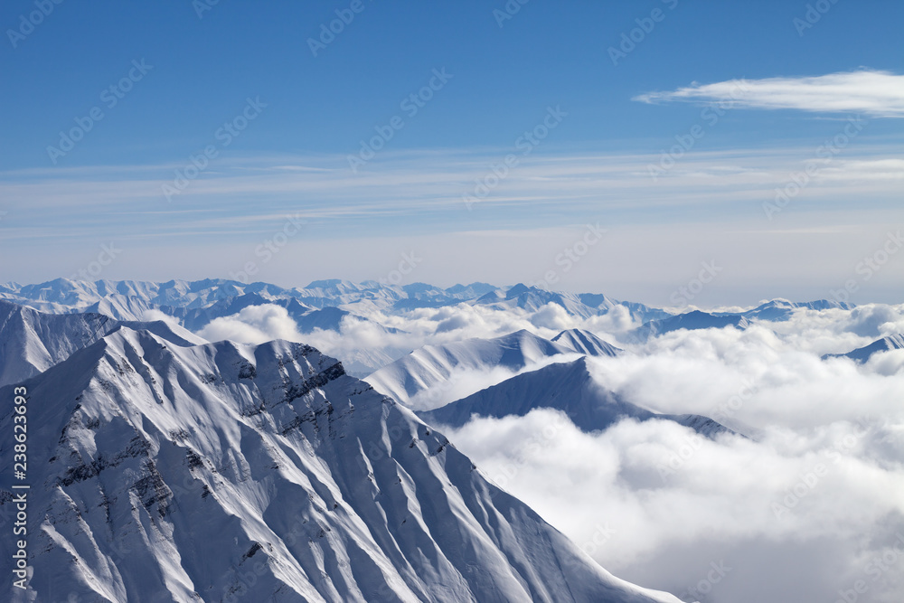 Snowy mountains in clouds and beautiful blue sky at nice winter day