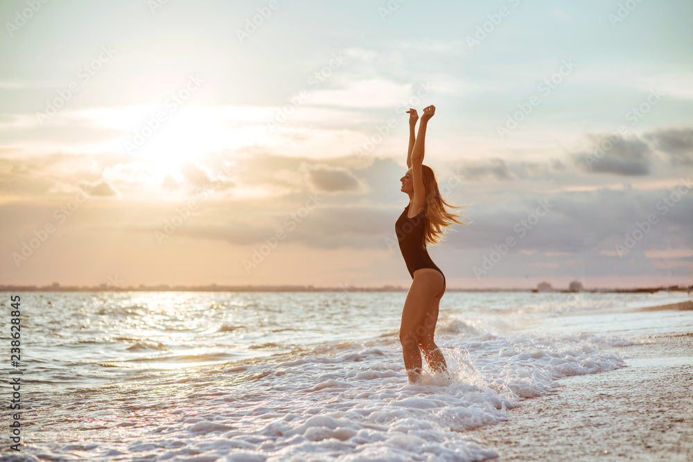 Outdoor lifestyle portrait of beautiful girl in black swimsuit. Young hipster woman play with her hair. She is happy. Sunny hot summer day at tropical ocean beach.