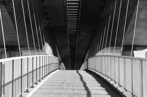 Rising path on the pedestrian bridge under the highway bridge in black and white with long shadows