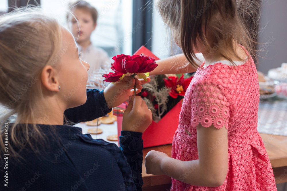 Sisters making floral Christmas decoration with red poinsettias. DIY seasonal crafts for kids. Sisters making floral Christmas decoration with red poinsettias. DIY seasonal crafts for kids.
