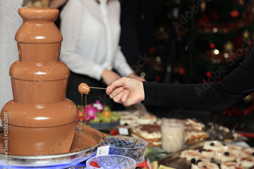 Dłoń kobiety zanurza owoce w czekoladzie.