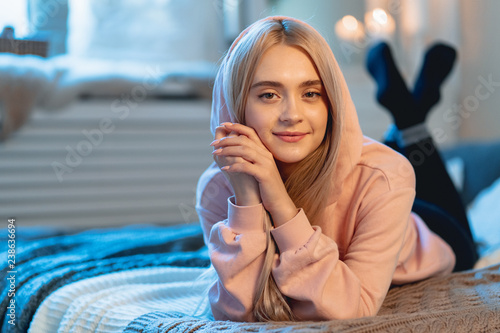 Young Cute Woman Lying Down On A Bed With Pillows Looking At Cam photo