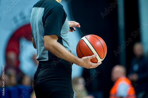 Basketball referee holding a basketball at a game in a crowded sports arena