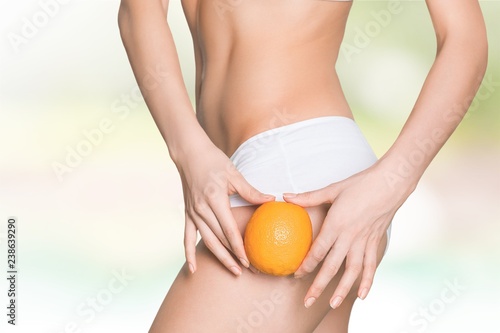 Female slender body in sport underwear holding orange on sea