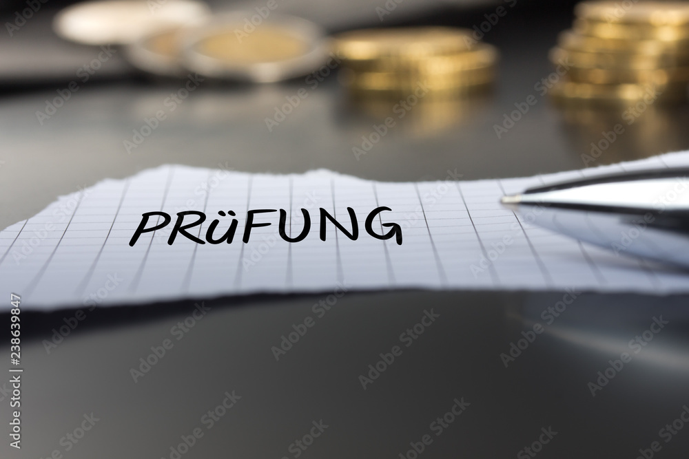 Prüfung auf einem Zettel mit Stift vor Geldmünzen Prüfung auf einem Zettel mit Stift vor Geldmünzen