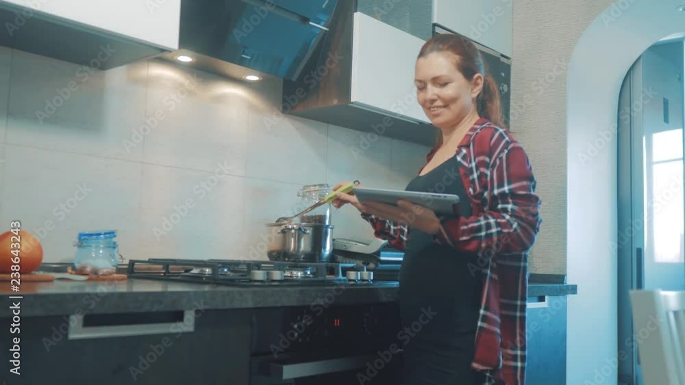 woman cooks soup pan in the kitchen prevents the water in the pot and looks at the recipe on the digital tablet. woman in the kitchen slow motion video. girl mom in the kitchen indoors preparing food woman cooks soup pan in the kitchen prevents the water in the pot and looks at the recipe on the digital tablet. woman in the kitchen slow motion video. girl mom in the kitchen indoors preparing food