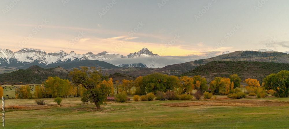 A distant snow capped mountain range in front of rolling green farm land