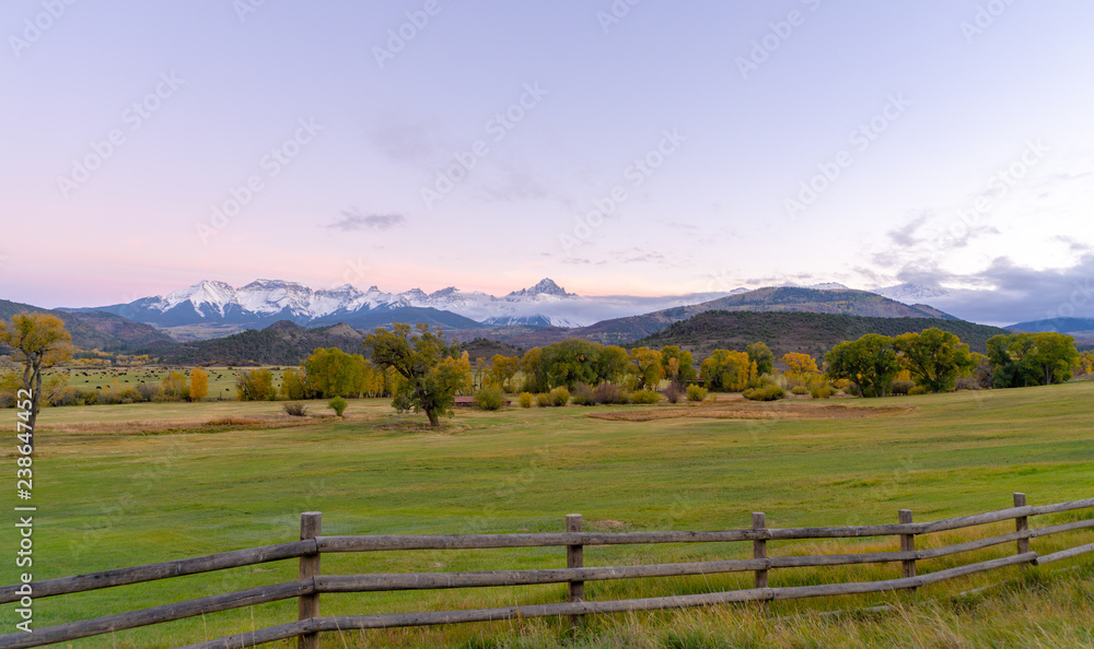 A distant snow capped mountain range in front of rolling green farm land