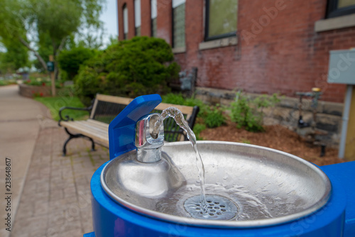 Drinking fountain in front of brick wall and path in small town.  Clean refreshing water flowing into vibrant blue bowl photo