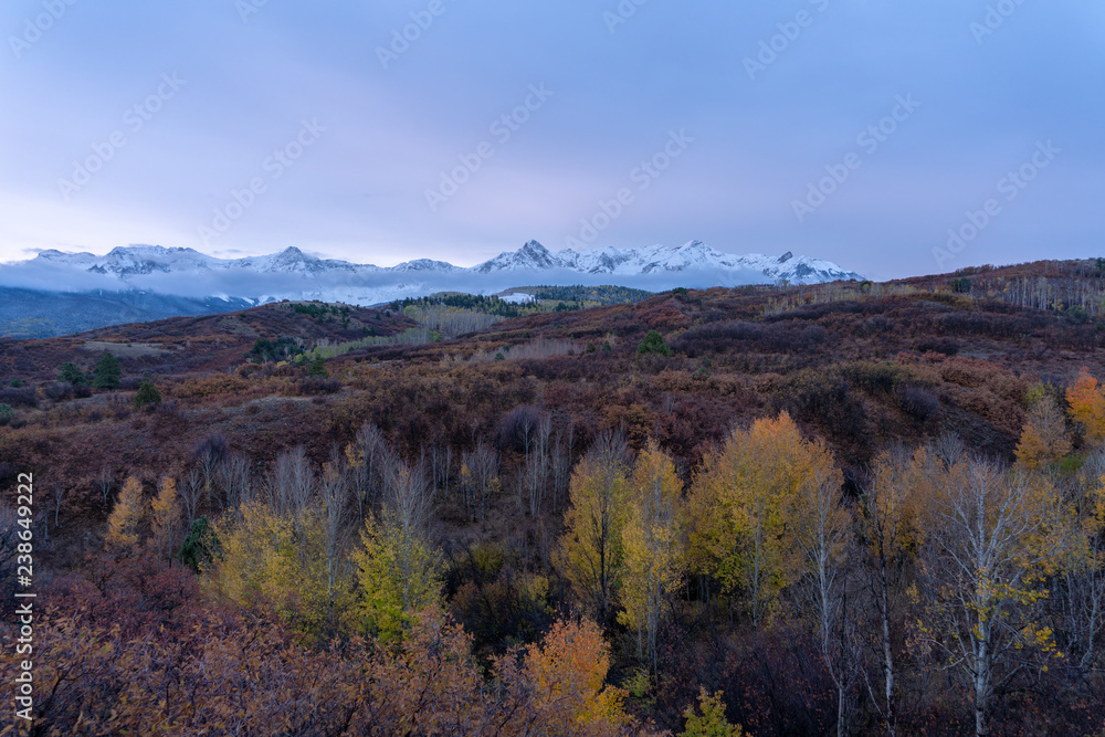 Snow capped peaks rise to meet pastel sunset colored skies in the Colorado Rockies