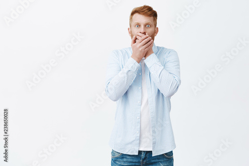 Man feeling regret saying secret. Portrait of shook and worried handsome mature man with ginger hair, covering mouth from shock and amazement being astonished, popping eyes at camera