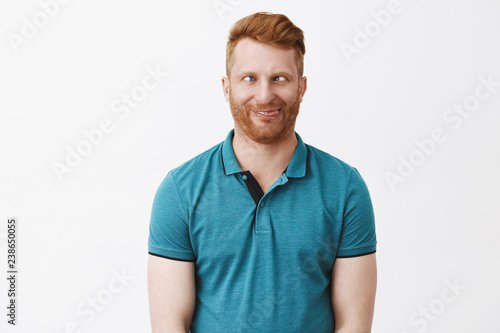 Waist-up shot of funny emotive and playful immature european male with ginger hair, squinting and rolling eyes aside, sticking out tongue, fooling around and aping, showing hilarious faces