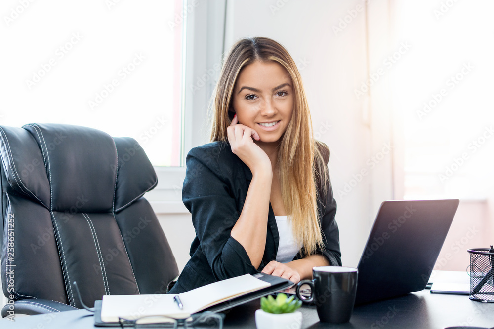 Portrait of a young stock-broker woman at office with laptop and notebook in front of her. Portrait of a young stock-broker woman at office with laptop and notebook in front of her.