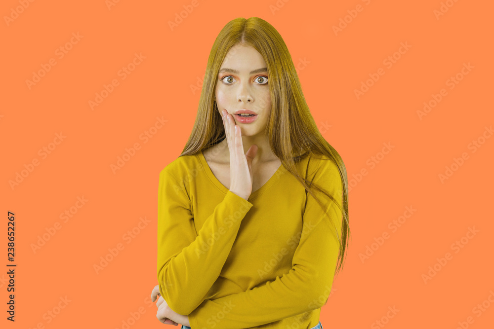 Red-haired young girl looks away with a scared facial expression propping up one hand on an isolated background Red-haired young girl looks away with a scared facial expression propping up one hand on an isolated background