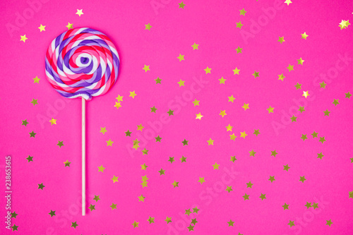 Big lollipop on solid pink background with golden sprinkles