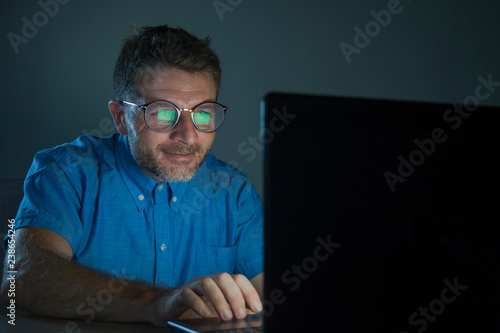 weird tidy and neat nerd man in big glasses and shirt working happy using internet on laptop computer late night in the dark looking stupid and ridiculous isolated background