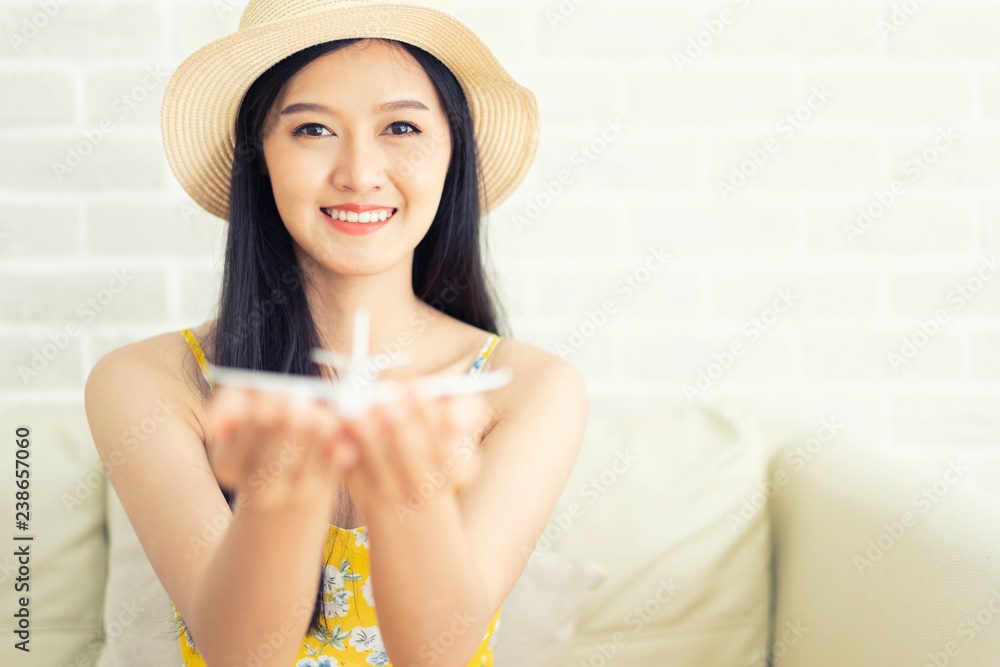Asian woman's hand flying toy plane .Beautiful young woman smiling planning vacation summer trip.she think and sitting sofa on brick background. Asian woman's hand flying toy plane .Beautiful young woman smiling planning vacation summer trip.she think and sitting sofa on brick background.