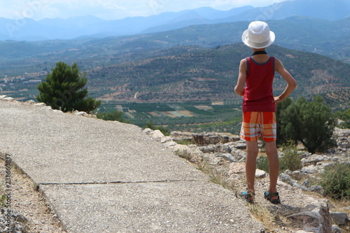Little tourist boy on the top of the hill look to the valley in Mycenae, Greece