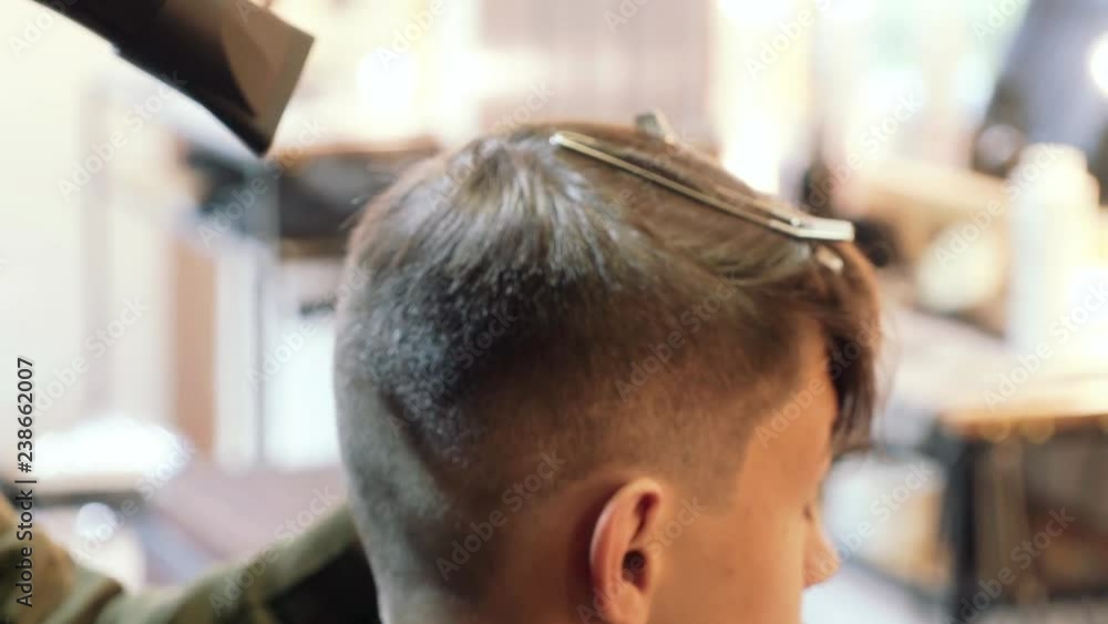 Hairdresser using hair dryer blows hair from a guy after hair cutting. Hairdresser using hair dryer blows hair from a guy after hair cutting.