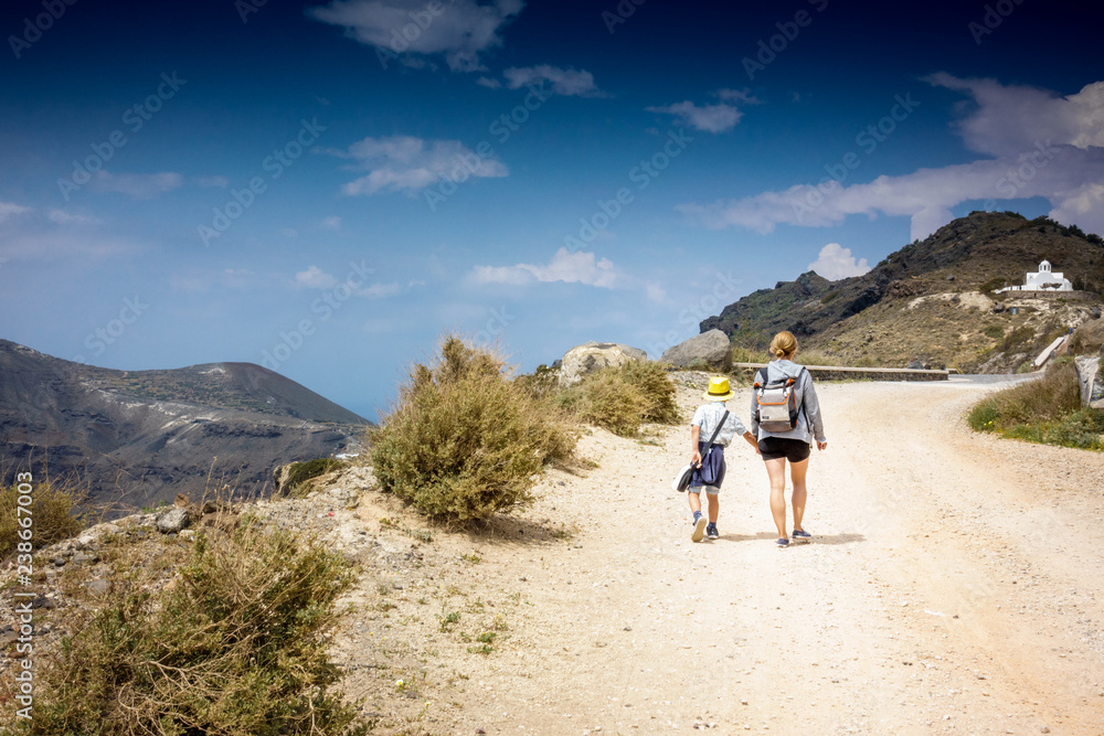 Mother with son walking on dirt road leading to mountain; Santorini island; Greece